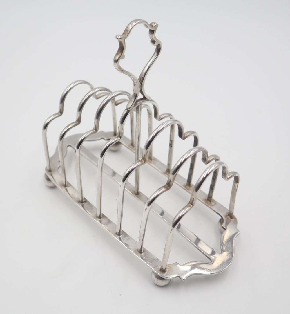 A silverplated toast rack featuring six arched wire slots, a central loop handle, and four small ball feet. View II