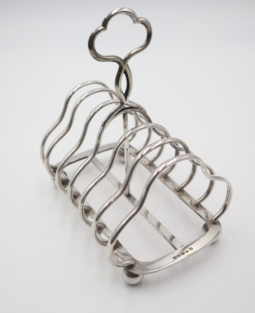 A silver-plated toast rack featuring six curved wire dividers, a central trefoil carrying handle, and four spherical ball feet. View V