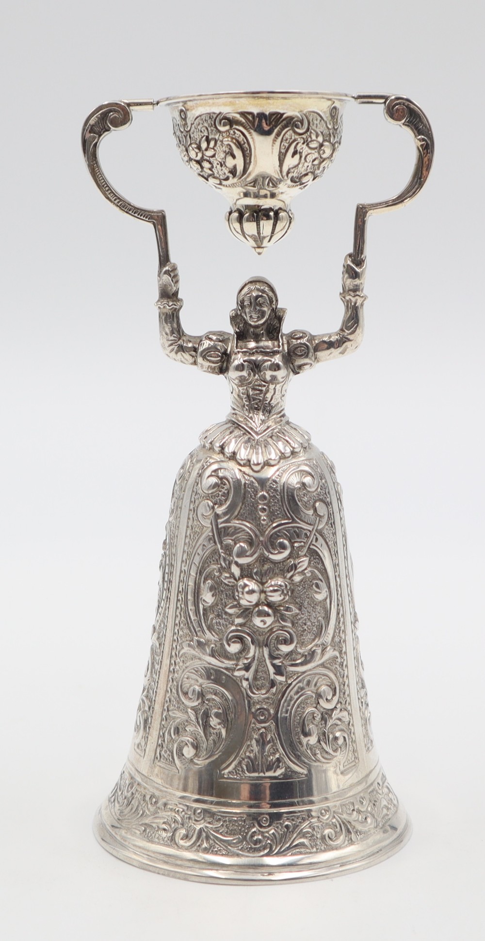An antique silver wager cup shaped as a female figure in a detailed floral skirt holding an articulated secondary cup overhead.