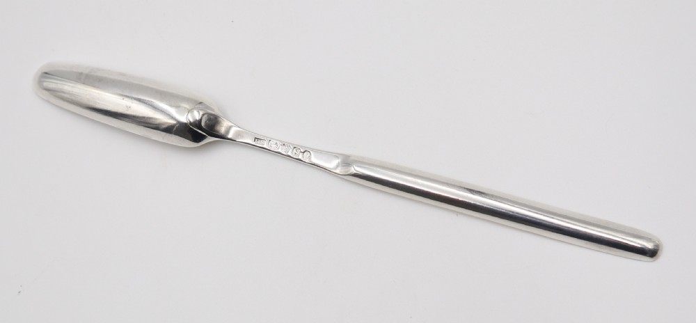 An elongated double-ended sterling silver marrow scoop with a narrow trough at one end and a broader trough at the other. View V
