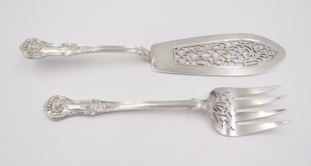 A two-piece set of silver fish servers comprising a pierced blade slice and a matching four-tined fork with decorative scroll handles.