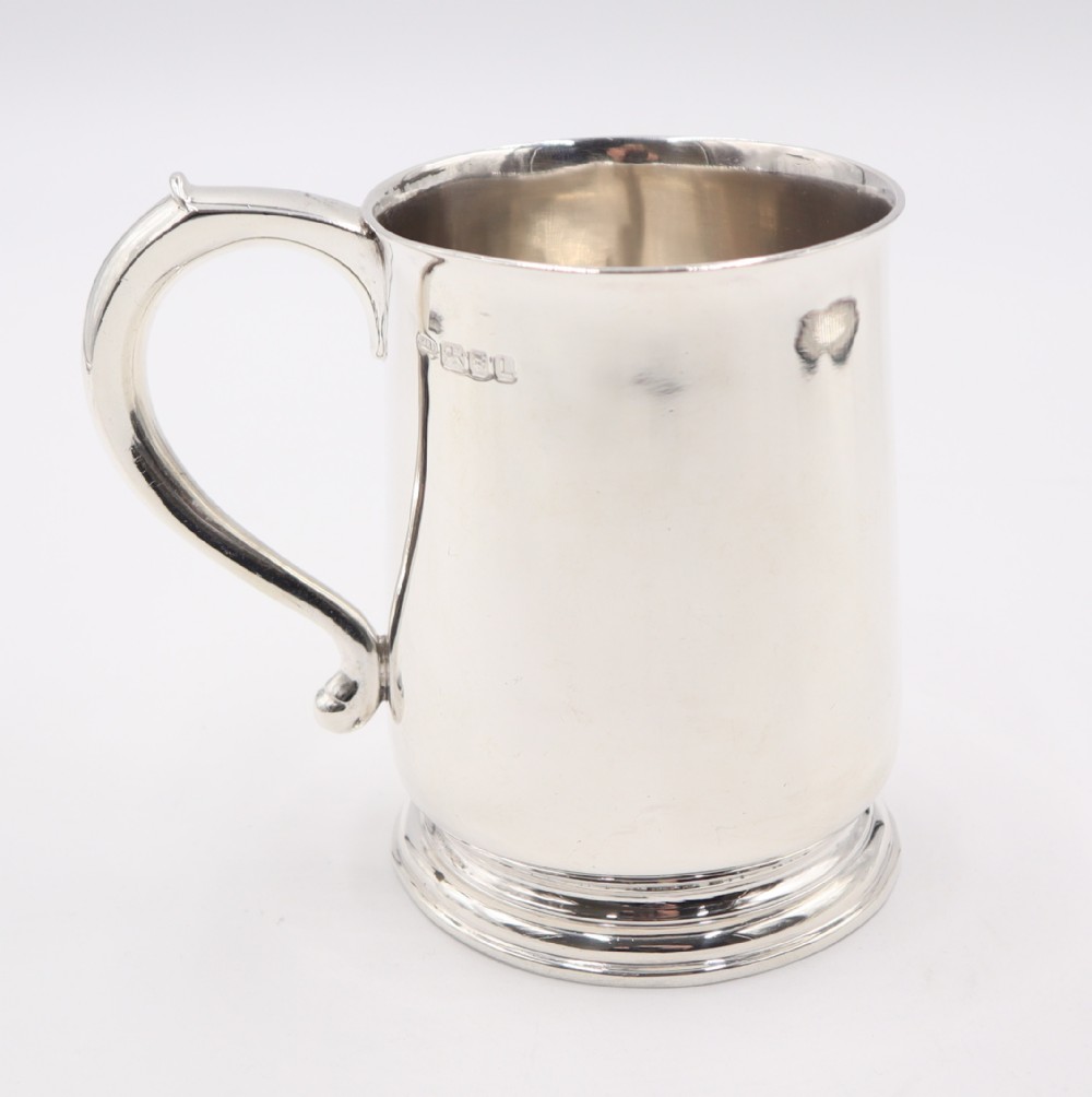 A polished sterling silver pint mug featuring a scroll handle, moulded circular base, and hallmarks stamped near the top rim against a plain white background.