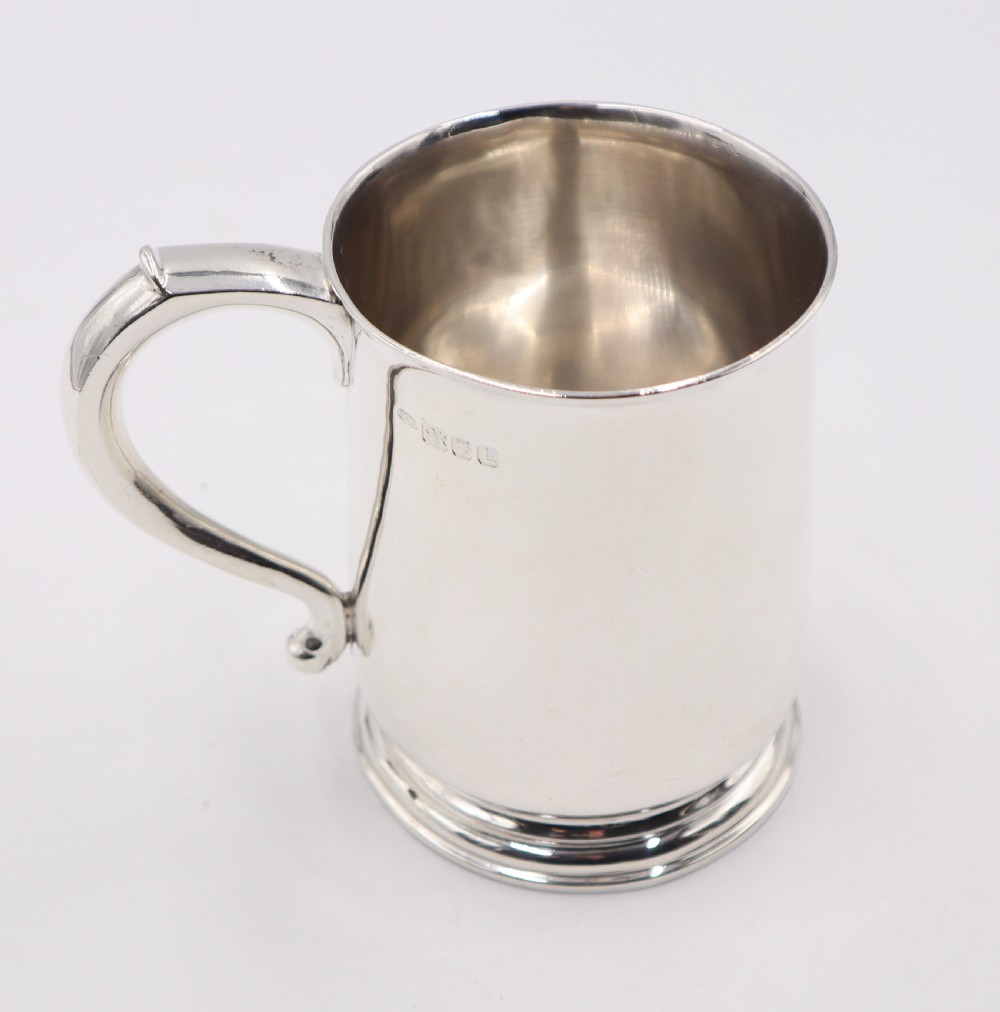 A polished sterling silver pint mug featuring a scroll handle, moulded circular base, and hallmarks stamped near the top rim against a plain white background. View III