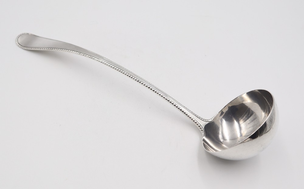An antique silver soup ladle featuring a beaded rim pattern along the long curved handle and a deep circular bowl.