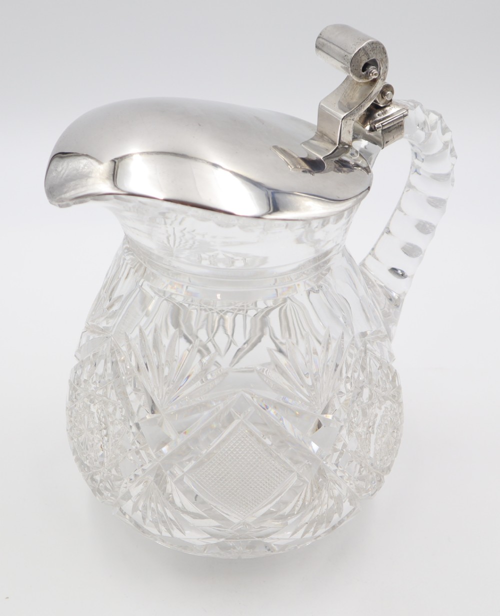 A pair of cut crystal glass jugs featuring silver mounts, hinged silver lids with scroll thumbpieces, and faceted crystal handles. View VIII