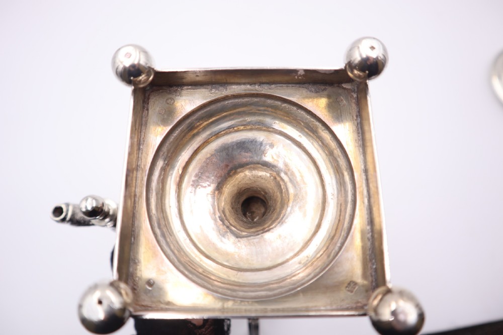 An antique silver tea urn featuring high loop handles, engraved floral bands, a front tap, and a square pedestal base supported by ball feet. View XI
