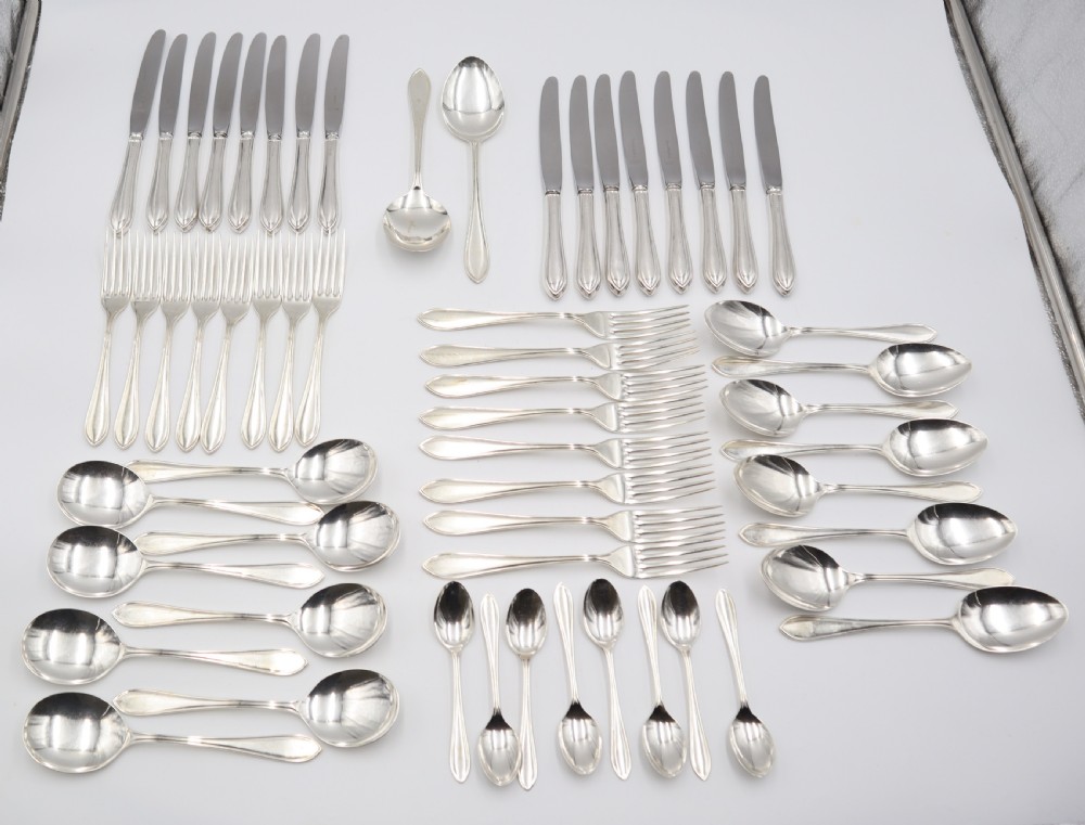 A comprehensive silver cutlery set containing dinner knives, forks, soup spoons, and dessert spoons laid out flat on a light grey background.