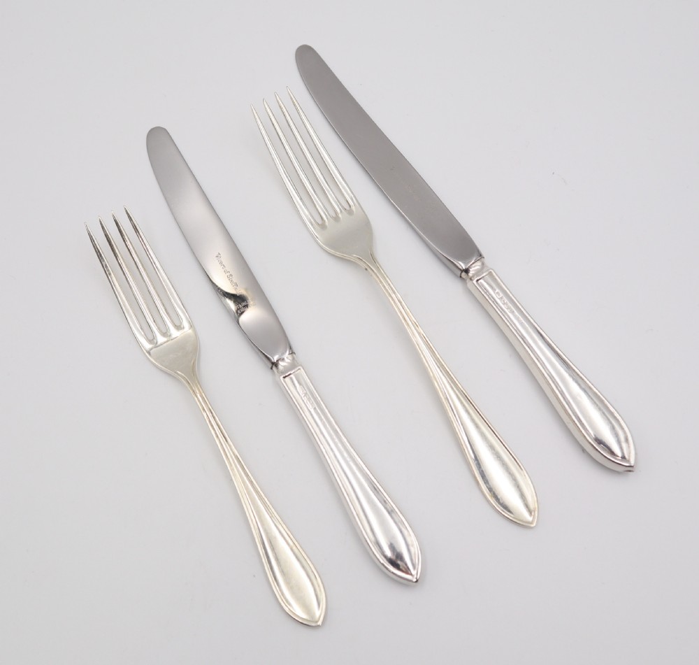 A comprehensive silver cutlery set containing dinner knives, forks, soup spoons, and dessert spoons laid out flat on a light grey background. View XI