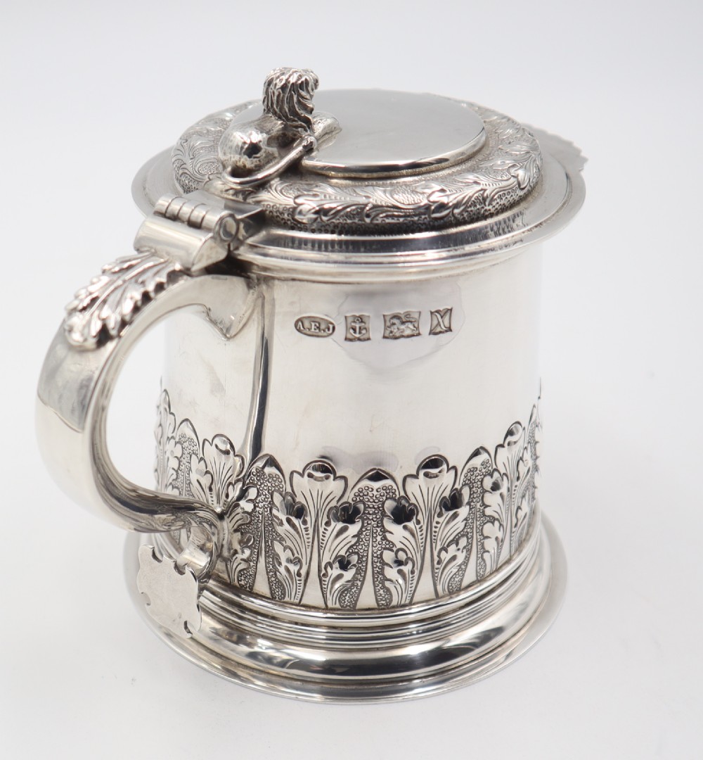A sterling silver lidded tankard featuring chased acanthus leaf decoration, a scroll handle, visible hallmarks, and a lion thumbpiece. View IX