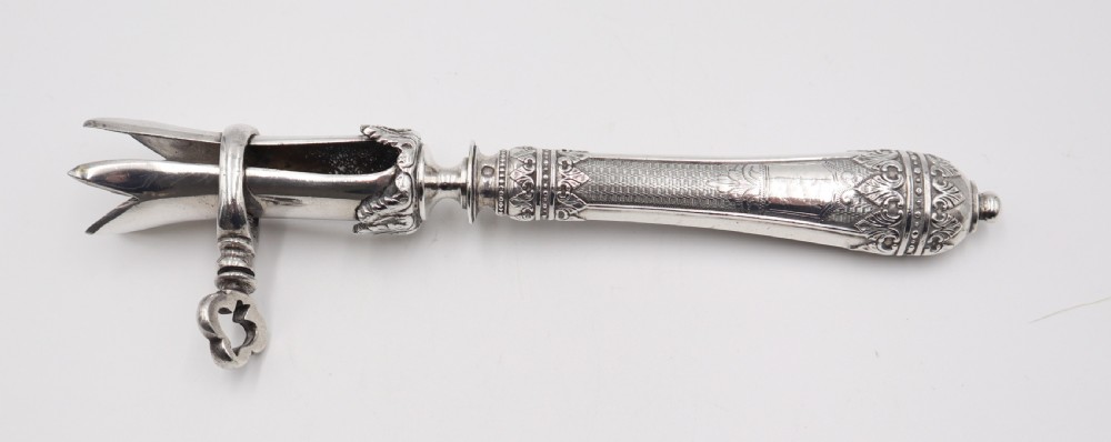 An antique silver ham bone holder featuring a decorated handle with chased leaf motifs, a threaded key screw, and adjustable pronged clamps. View II