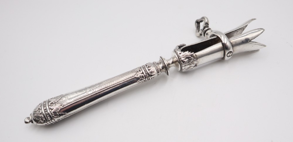 An antique silver ham bone holder featuring a decorated handle with chased leaf motifs, a threaded key screw, and adjustable pronged clamps. View III