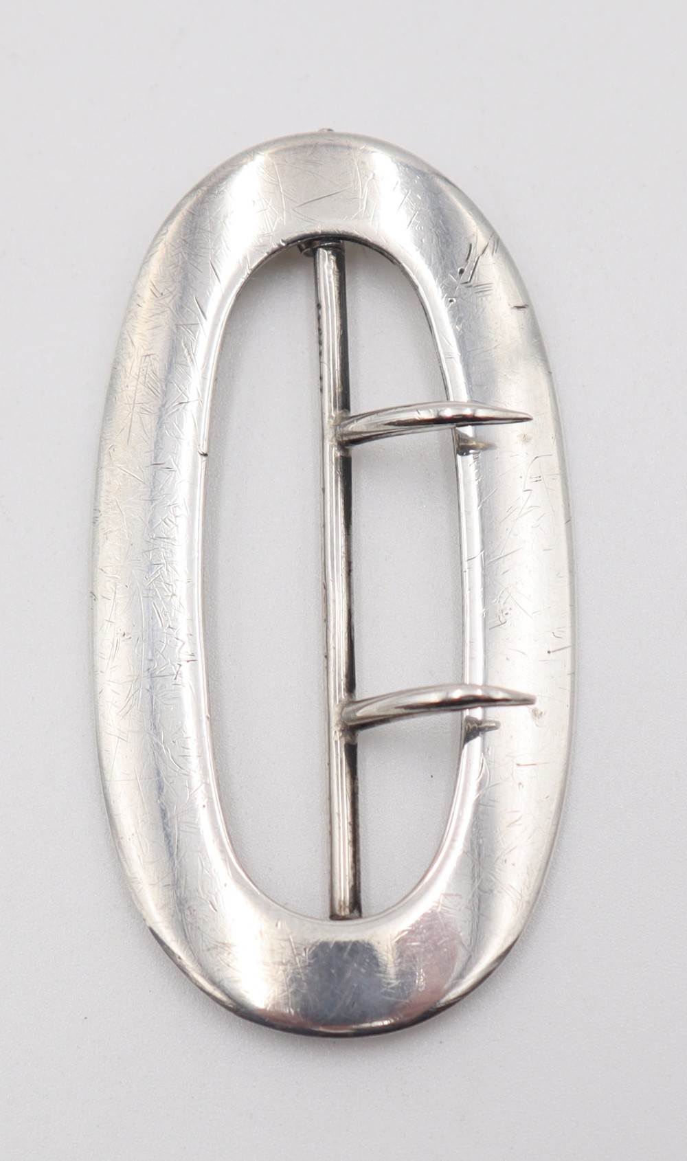 An oval sterling silver buckle featuring a central vertical bar with two pointed prongs.