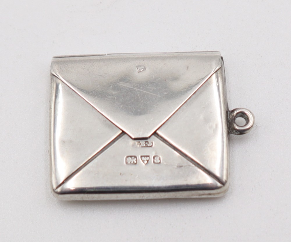 A small sterling silver stamp case designed in the shape of a sealed letter envelope with visible hallmarks.