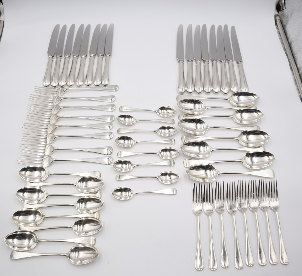 A complete antique silver cutlery set comprising table knives, forks, soup spoons, dessert spoons, and teaspoons arranged neatly on a white background.