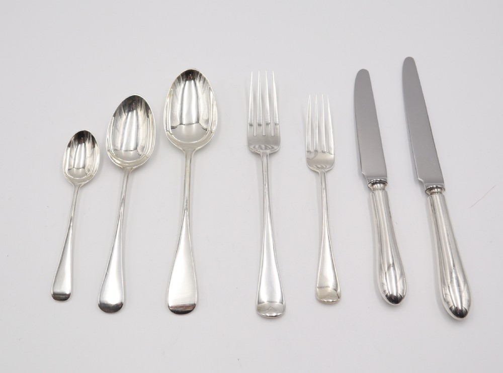 A complete antique silver cutlery set comprising table knives, forks, soup spoons, dessert spoons, and teaspoons arranged neatly on a white background. View II
