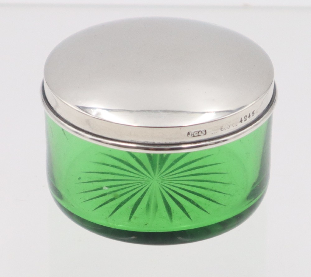 A circular green glass vanity jar featuring a cut starburst pattern on the base and a fitted polished silver lid.