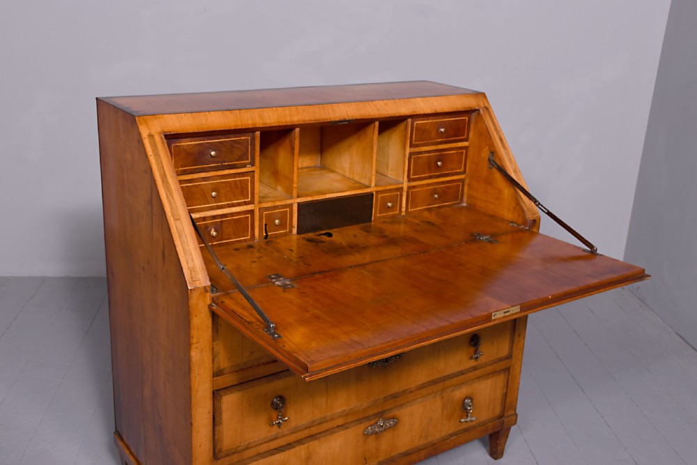 A 19th-century blonde walnut slant-front bureau featuring rosewood inlay, a central star motif on the lid, and three long drawers with decorative metal handles. View VI