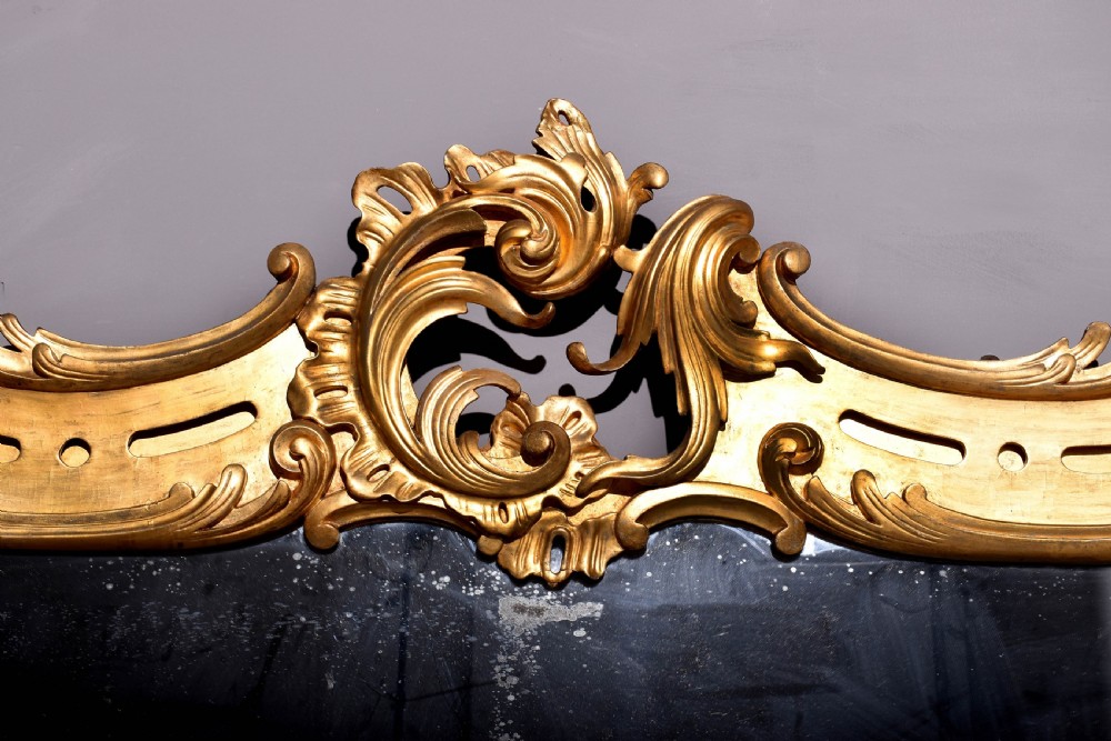 A William IV gilded overmantel mirror with Rococo scrollwork and carved acanthus leaf cresting. View II