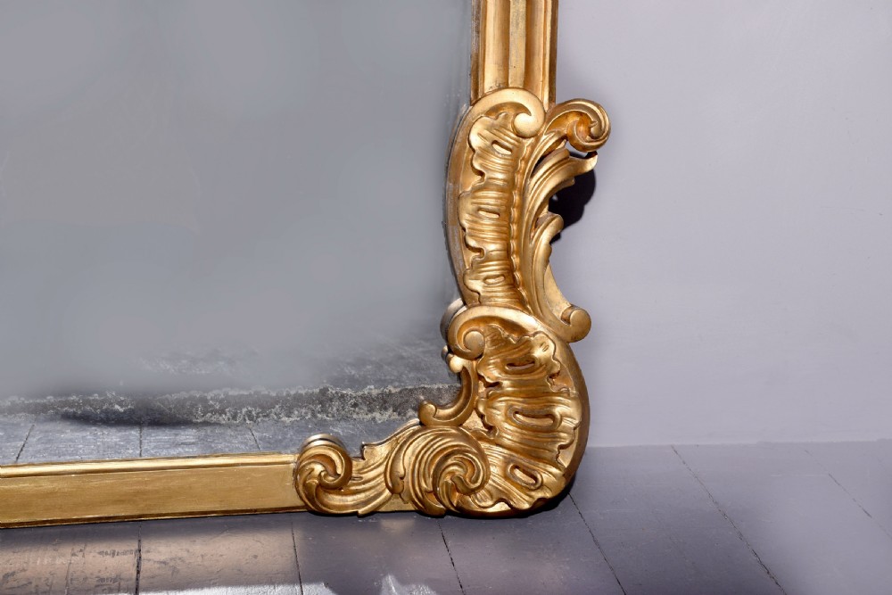A William IV gilded overmantel mirror with Rococo scrollwork and carved acanthus leaf cresting. View IV