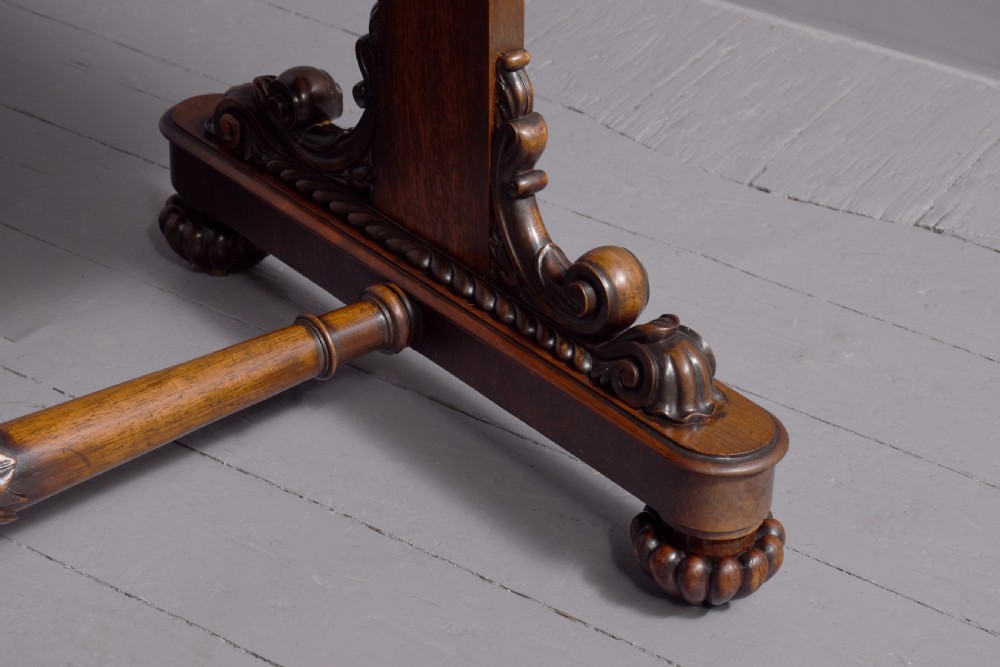 A William IV rosewood library table featuring a rectangular top, two frieze drawers, carved scroll brackets, end pedestal supports, and a turned central stretcher. View III