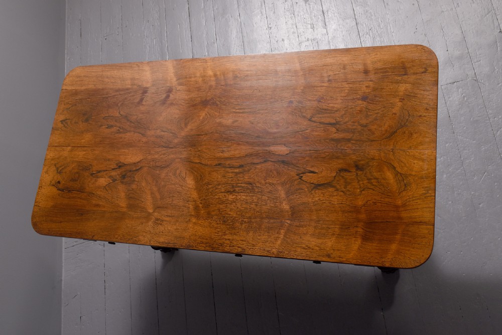 A William IV rosewood library table featuring a rectangular top, two frieze drawers, carved scroll brackets, end pedestal supports, and a turned central stretcher. View V