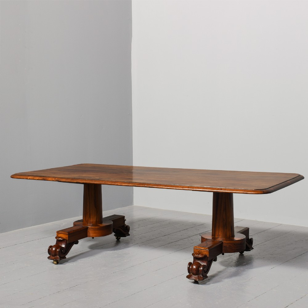 A low rectangular rosewood coffee table featuring twin turned pedestal supports, carved scroll feet, and brass castors.