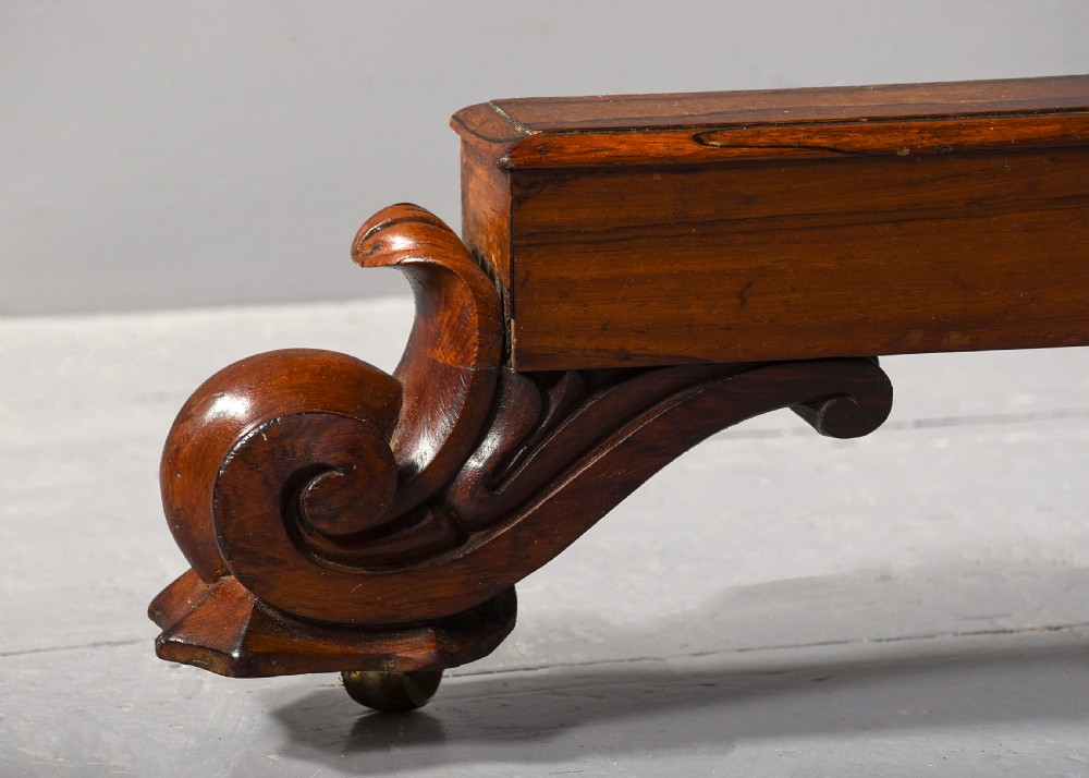 A low rectangular rosewood coffee table featuring twin turned pedestal supports, carved scroll feet, and brass castors. View VI