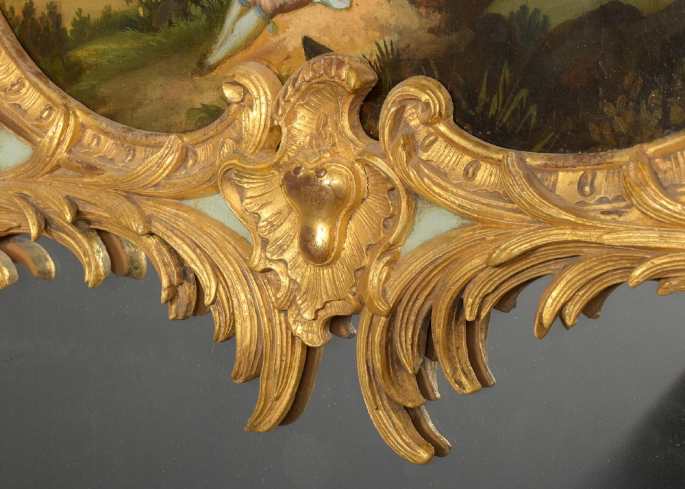 A large French trumeau wall mirror featuring a pale sage green painted panel base, elaborate gold gilt scrollwork framing, an upper oval pastoral oil painting, and a lower rectangular mirror glass. View V