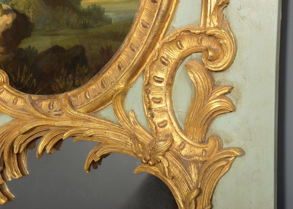 A large French trumeau wall mirror featuring a pale sage green painted panel base, elaborate gold gilt scrollwork framing, an upper oval pastoral oil painting, and a lower rectangular mirror glass. View IX