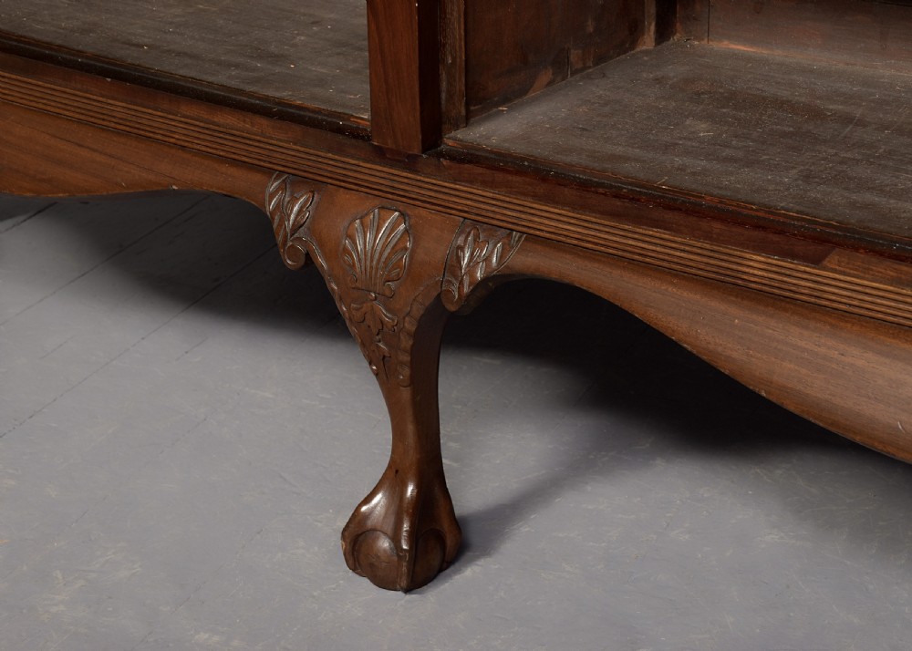 A wide dark mahogany open bookcase featuring twin double bays with multiple shelves, decorative inlay on the frieze, carved shell motifs on the lower apron, and cabriole legs ending in ball and claw feet. View VI
