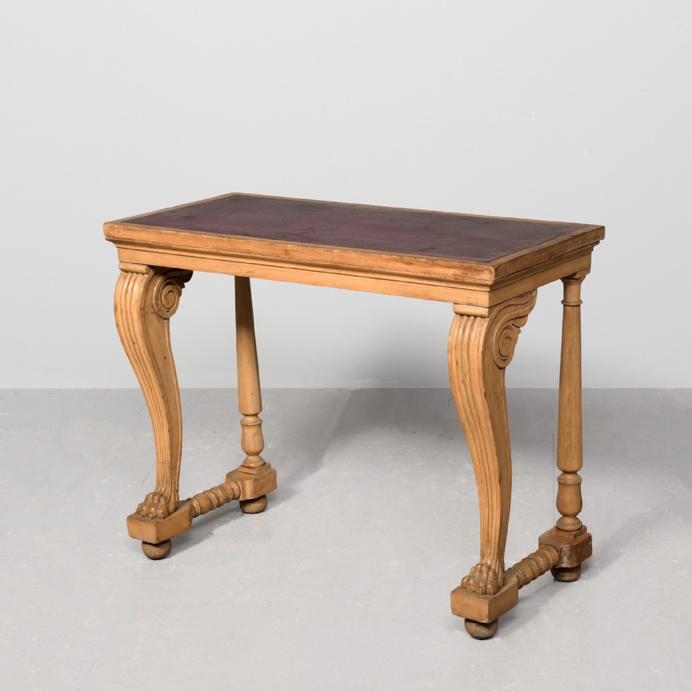 A Regency light wood console table featuring an inset reddish leather top, front scroll-carved legs with paw feet, and turned rear supports.