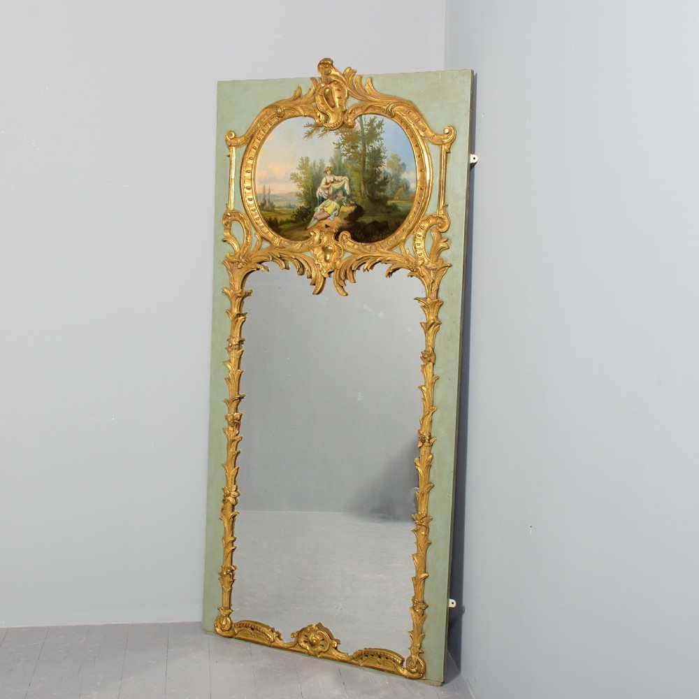 A large French trumeau wall mirror featuring a pale sage green painted panel base, elaborate gold gilt scrollwork framing, an upper oval pastoral oil painting, and a lower rectangular mirror glass.