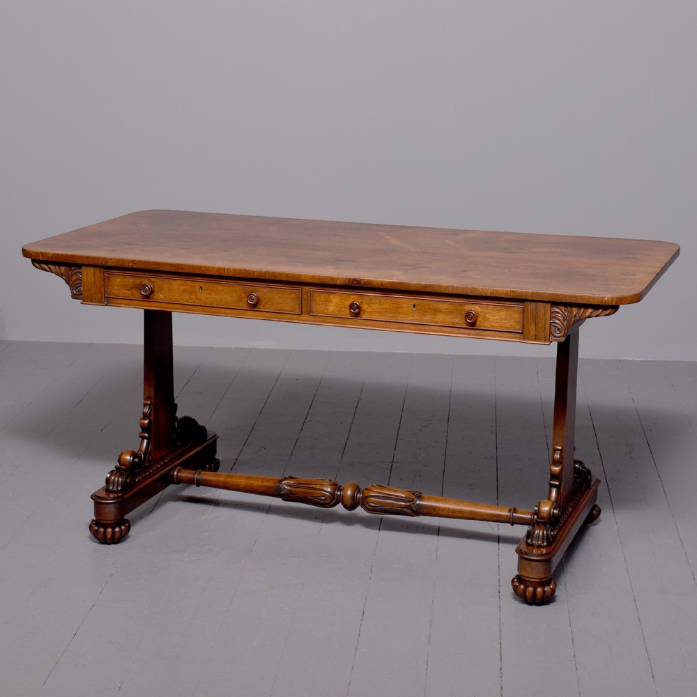 A William IV rosewood library table featuring a rectangular top, two frieze drawers, carved scroll brackets, end pedestal supports, and a turned central stretcher.