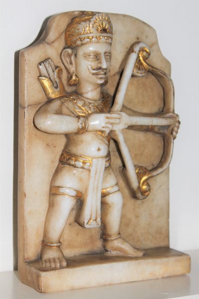 fig 1. A carved white marble relief panel depicting the Hindu mythological archer Arjuna holding a bow, accented with gold leaf details.