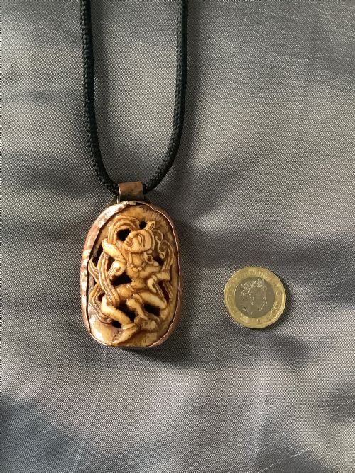 A VERY FINELY CARVED BONE INDIAN PENDANT ENCASED IN A METAL FRAME