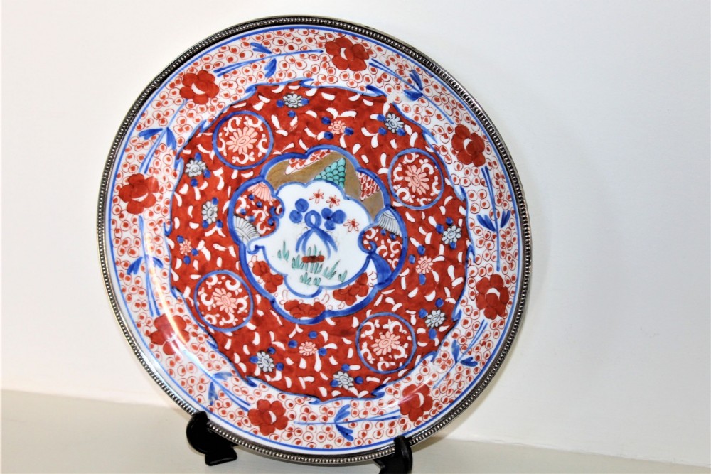 A circular Chinese Imari porcelain charger featuring hand-painted iron-red and underglaze blue floral patterns with a beaded metal outer rim.