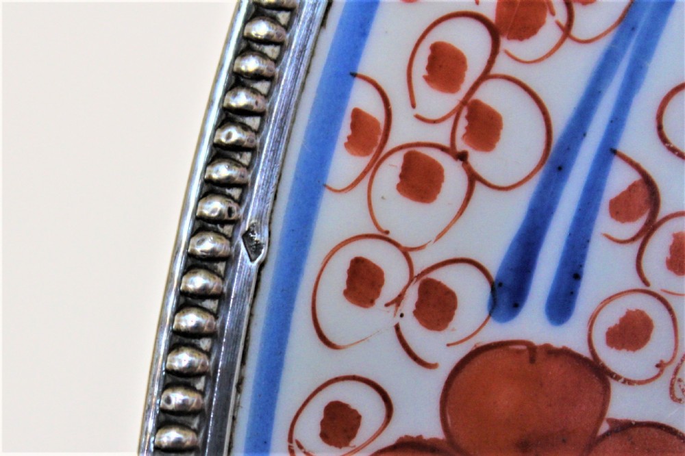 A circular Chinese Imari porcelain charger featuring hand-painted iron-red and underglaze blue floral patterns with a beaded metal outer rim. View V