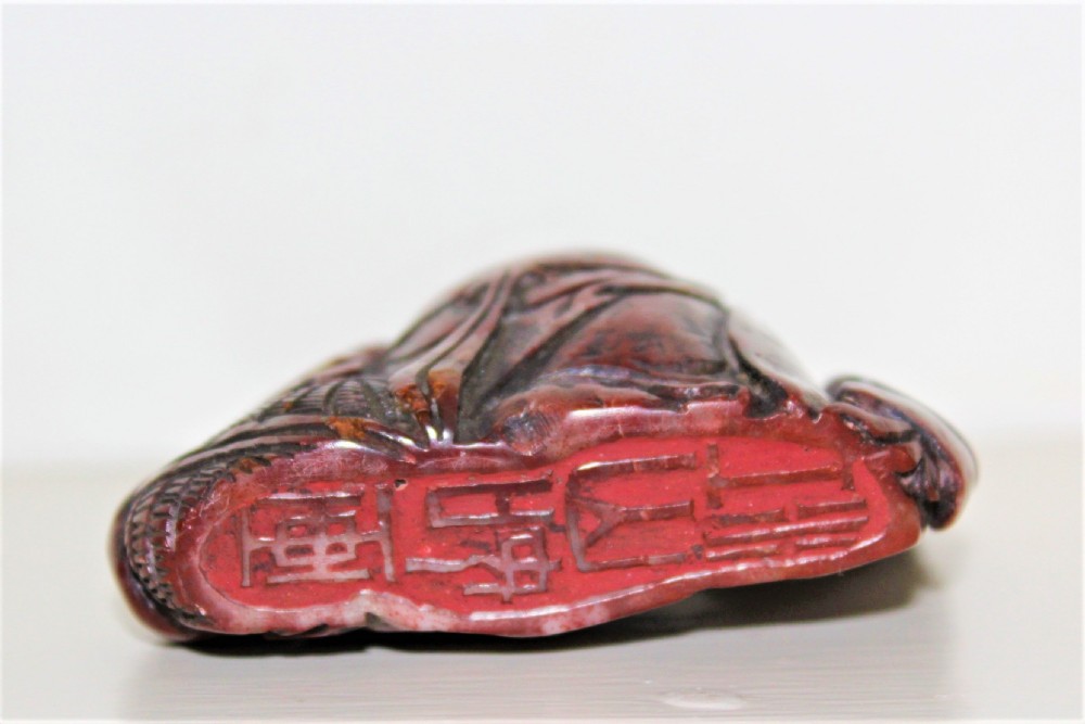 A carved reddish-brown soapstone desk seal depicting a seated, smiling Buddha figure with draped robes. View II