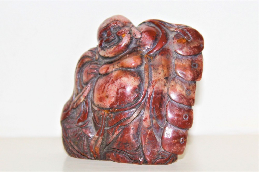 A carved reddish-brown soapstone desk seal depicting a seated, smiling Buddha figure with draped robes. View III