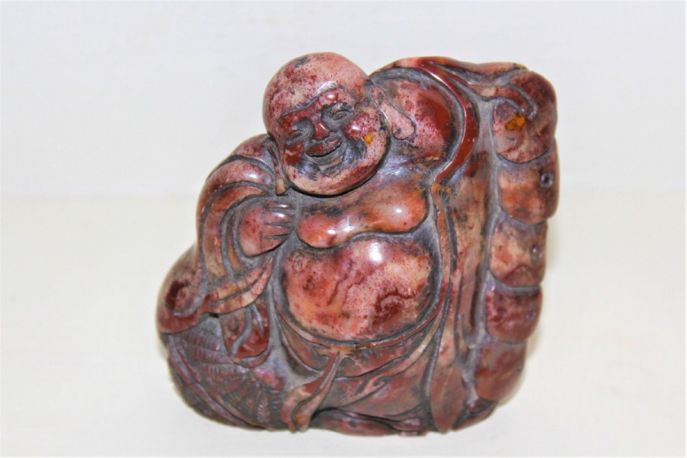 A carved reddish-brown soapstone desk seal depicting a seated, smiling Buddha figure with draped robes.