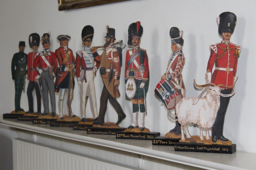 A set of nine hand-painted wooden cut-out figures depicting historic British military officers and soldiers standing on black wooden plinths.