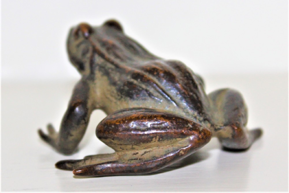 A small cast bronze study of a crouching frog displaying a patinated surface with subtle green oxidisation.