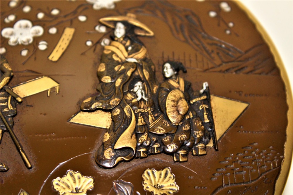 A circular brown bronze box lid decorated with high relief figures under cherry blossoms highlighted in gold and silver metal inlay. View IV