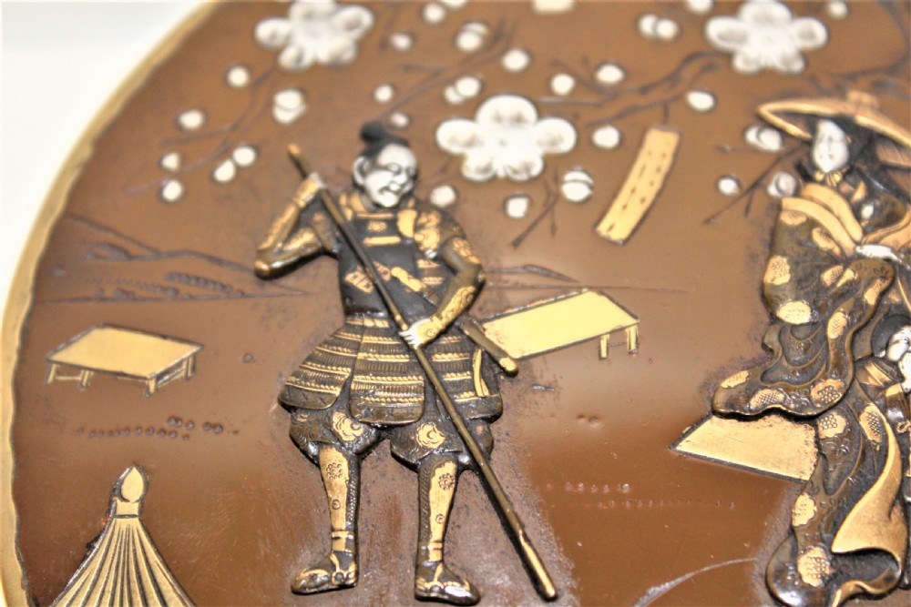 A circular brown bronze box lid decorated with high relief figures under cherry blossoms highlighted in gold and silver metal inlay. View V