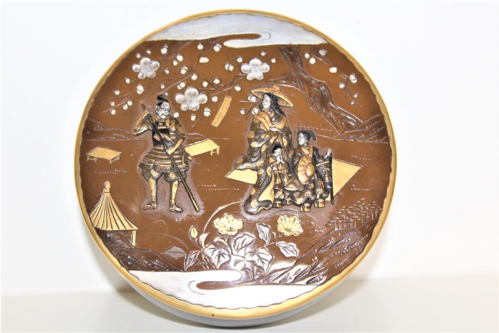 A circular brown bronze box lid decorated with high relief figures under cherry blossoms highlighted in gold and silver metal inlay. View IX