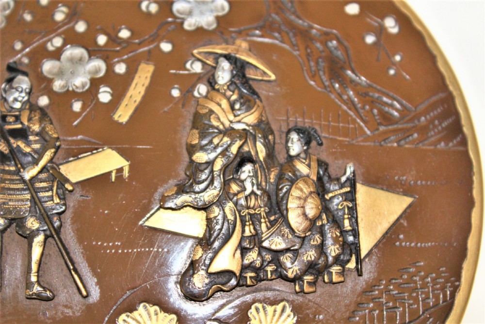 A circular brown bronze box lid decorated with high relief figures under cherry blossoms highlighted in gold and silver metal inlay. View X