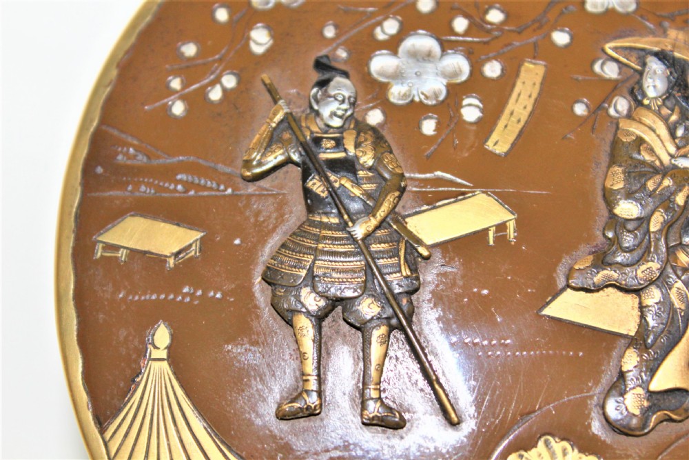 A circular brown bronze box lid decorated with high relief figures under cherry blossoms highlighted in gold and silver metal inlay. View XI