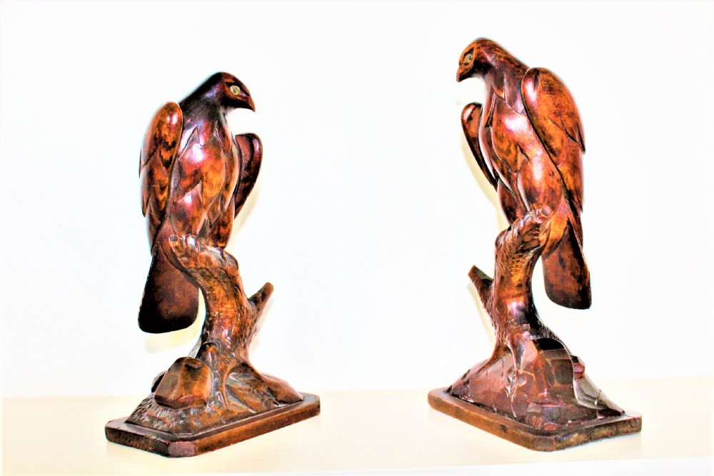 A pair of carved brown wooden eagle sculptures perched on tree branches atop rectangular bases, featuring detailed feathering and penwork.