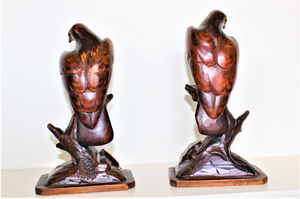 A pair of carved brown wooden eagle sculptures perched on tree branches atop rectangular bases, featuring detailed feathering and penwork. View II