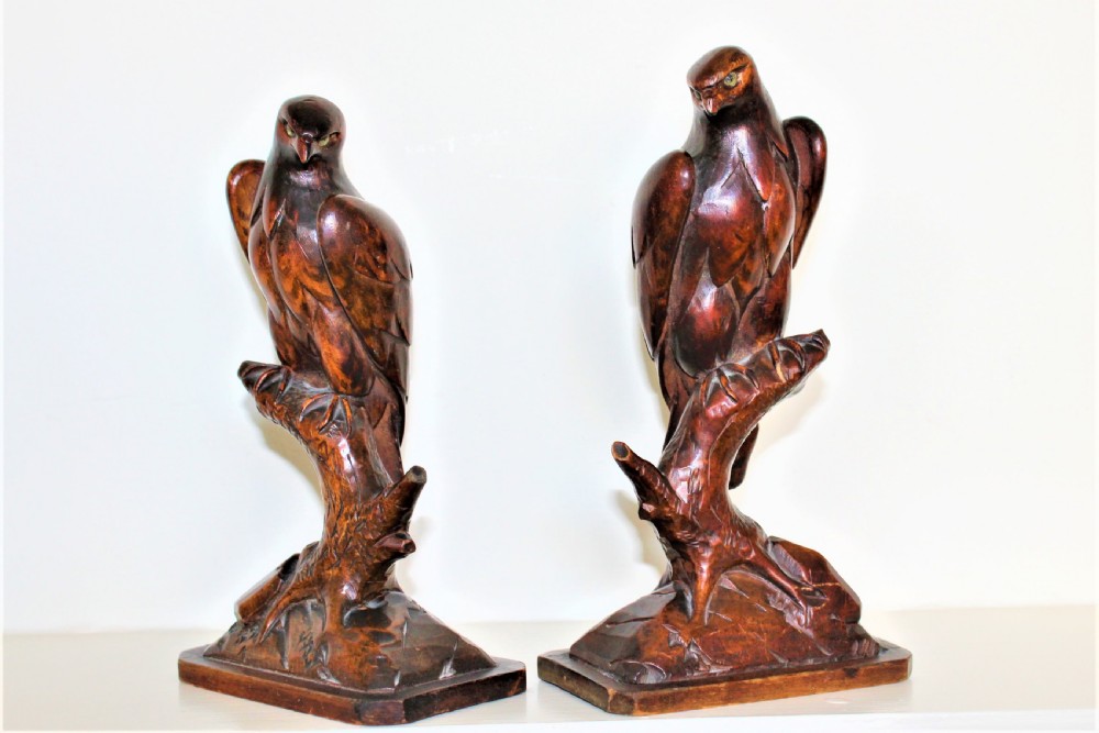 A pair of carved brown wooden eagle sculptures perched on tree branches atop rectangular bases, featuring detailed feathering and penwork. View III